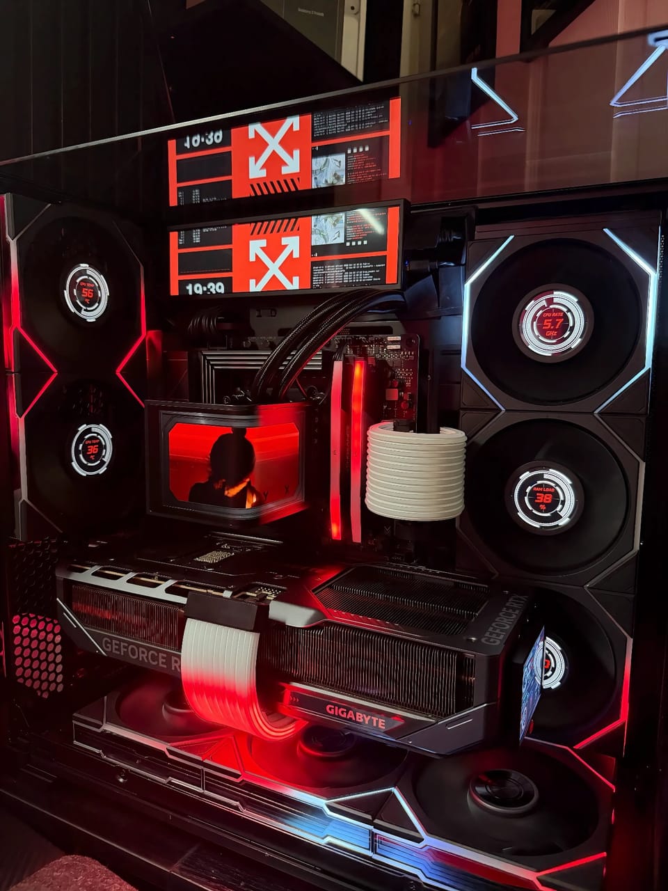 Góc máy của Nguyen Nick: Dàn PC tản nhiệt nước tông đen đỏ phong cách cyberpunk, card Gigabyte RTX, quạt hiển thị thông số và hai màn hình thanh phía trên.