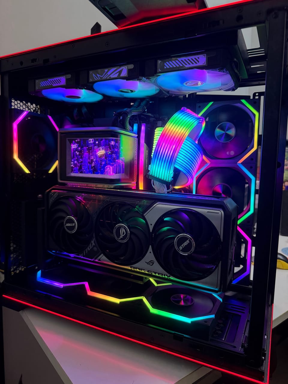 Góc máy của Thanh Tin: Dàn PC case kính đen rực rỡ RGB với card ASUS ROG Strix, tản nước màn hình LCD và cáp nguồn cầu vồng.