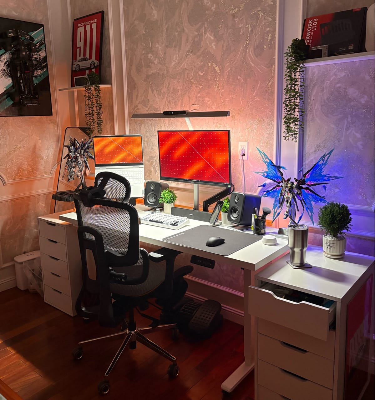 Setup góc máy của Wy: Góc máy bàn nâng hạ trắng, màn hình kèm laptop, loa đôi, mô hình Gundam phát sáng và cây xanh trang trí.