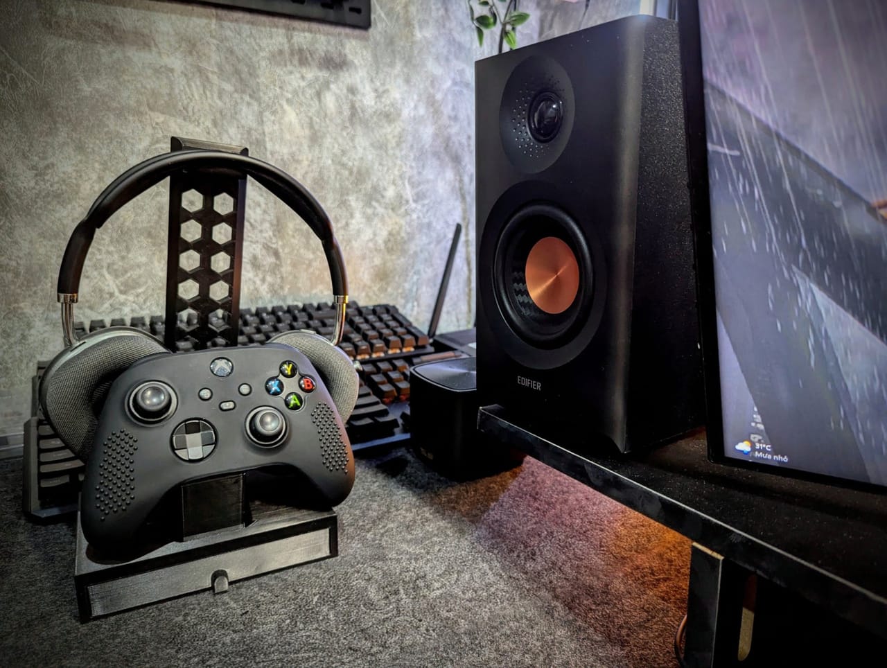 Góc máy của W1zardne: Góc setup tông đen với tay cầm Xbox và tai nghe trên giá in 3D, loa Edifier, bàn phím cơ phía sau và màn hình bên phải.