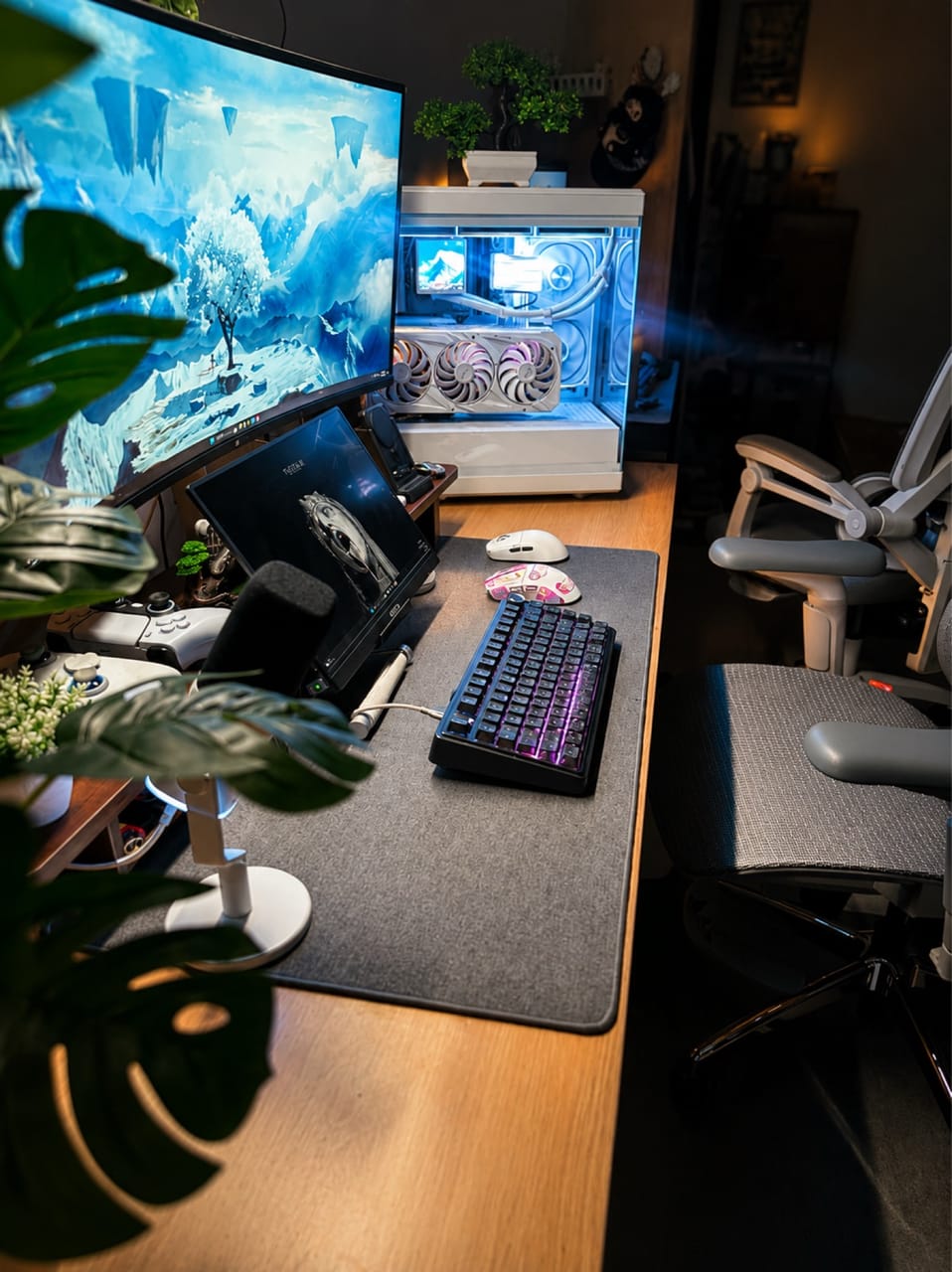 Góc máy của Bảo Lâm: Góc setup bàn gỗ với PC case trắng tản nhiệt nước đèn xanh, màn hình cong, bàn phím LED tím, hai chuột và nhiều cây xanh.