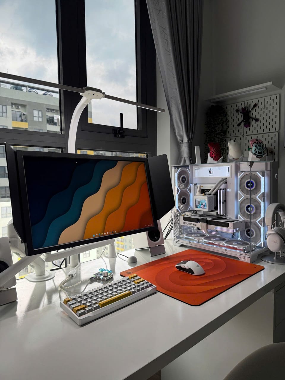 Góc máy của zokie: Góc máy tông trắng gọn gàng bên cửa sổ, có PC case kính trong suốt, bàn phím cơ, lót chuột cam và tai nghe trắng.