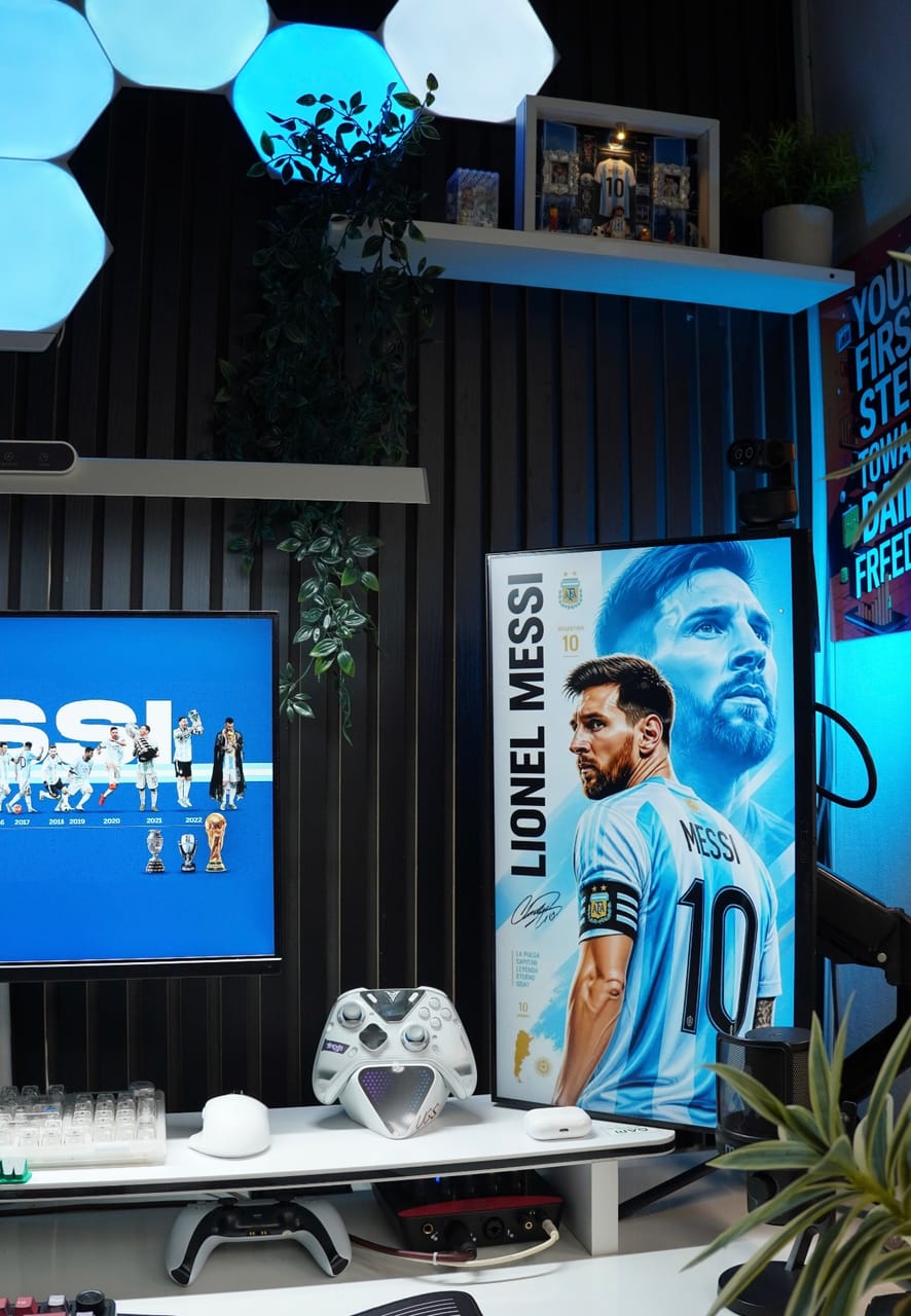 Góc máy của Drake nè: Góc setup tông xanh trắng với đèn LED lục giác, hai màn hình, bàn phím trong suốt, tay cầm trắng và cây xanh trang trí.