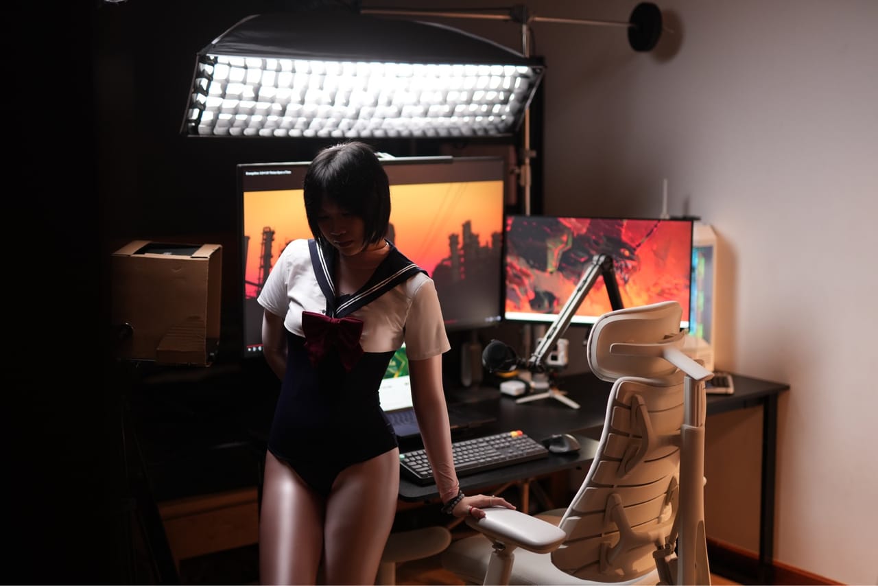 Setup góc máy của Bảo Dạy Edit: Góc máy bàn đen với hai màn hình, micro cần, ghế công thái học trắng và đèn studio lớn phía trên.