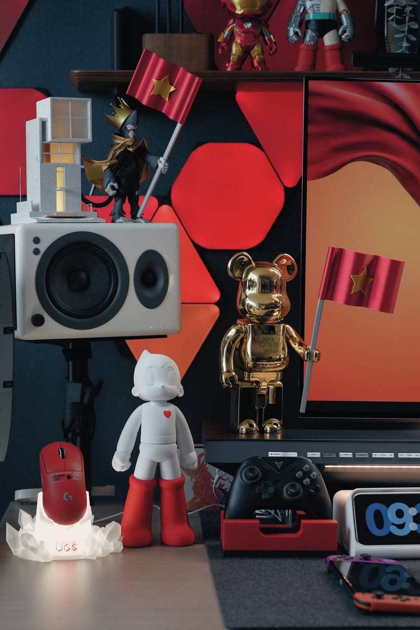 Góc máy của Xung Quanh Trung: Góc setup tông đỏ trắng đen với mô hình Astro Boy, gấu vàng cầm cờ Việt Nam, loa trắng, chuột Logitech đỏ và tay cầm chơi game.