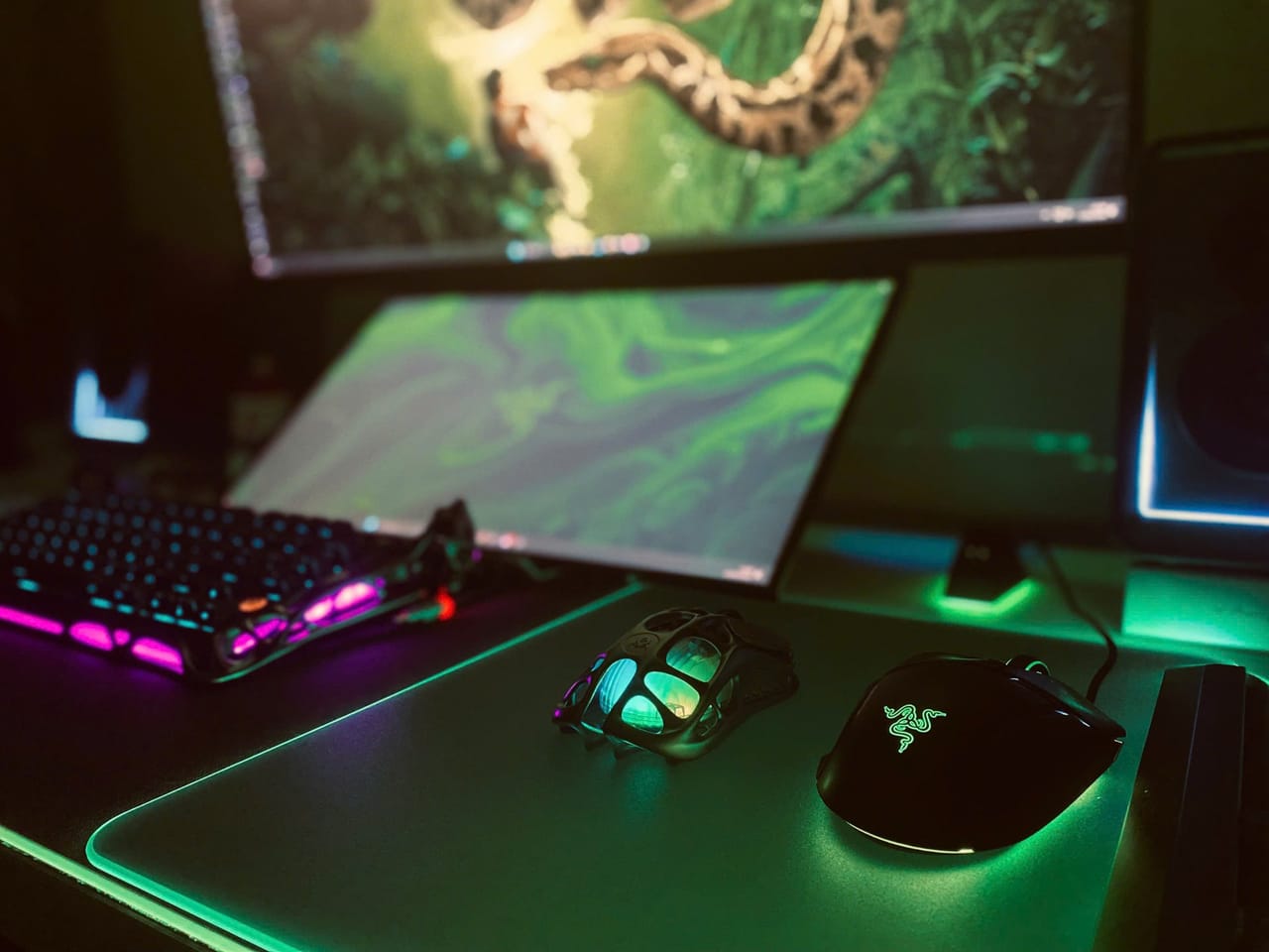 Góc máy của Tony Quân: Góc setup tối với đèn RGB xanh lá và hồng, có hai màn hình, bàn phím cơ, hai chuột và lót chuột phát sáng.