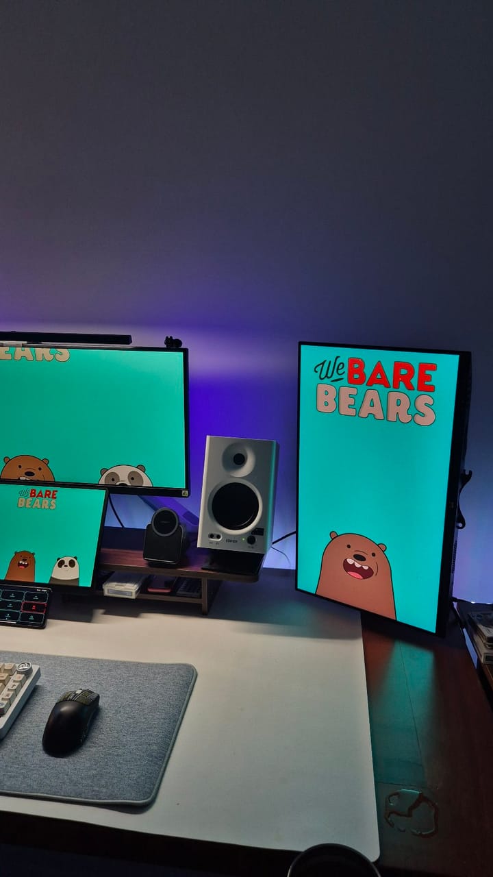 Góc máy của Khánh99: Góc máy ba màn hình dùng hình nền We Bare Bears xanh ngọc, có loa trắng, đèn nền tím, bàn phím cơ và chuột đen trên lót xám.