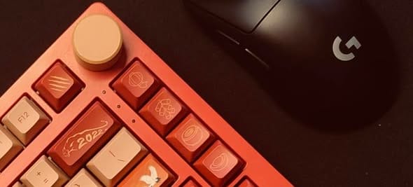 Góc máy của 0racle: Bàn phím cơ tông cam đỏ với keycap chủ đề năm 2022 và núm xoay màu be, đặt cạnh chuột Logitech màu đen trên mặt bàn tối.