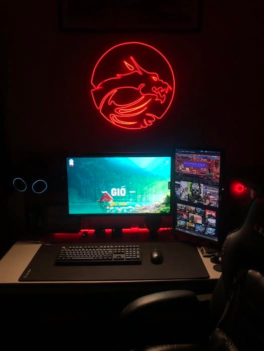 Góc máy của 0racle: Góc máy tối với đèn neon rồng đỏ trên tường, hai màn hình đặt ngang và dọc, bàn phím cơ, chuột và lót chuột lớn.