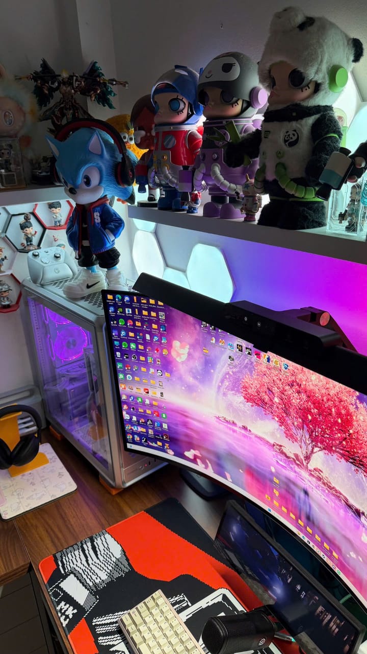 Góc máy của khachoang: Góc setup trắng ánh đèn RGB tím hồng, màn hình cong, case kính và kệ trưng bày nhiều figure, mô hình Sonic nổi bật.