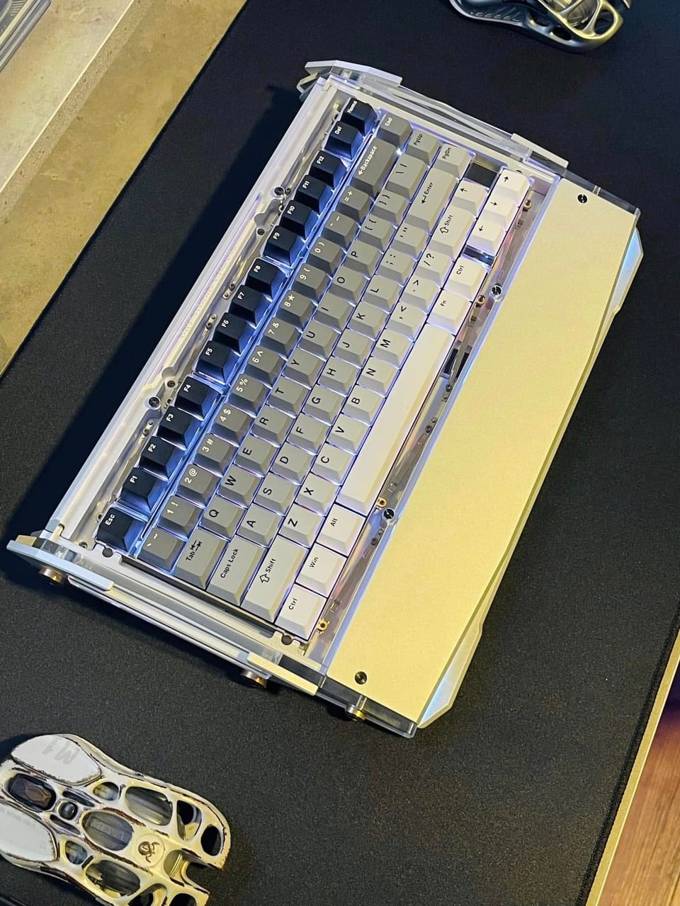 Góc máy của Hieu KU TO: Bàn phím cơ vỏ acrylic trong suốt kèm kê tay nhôm, keycap xám trắng, đèn nền xanh tím, đặt trên lót chuột đen cạnh hai chuột tổ ong.