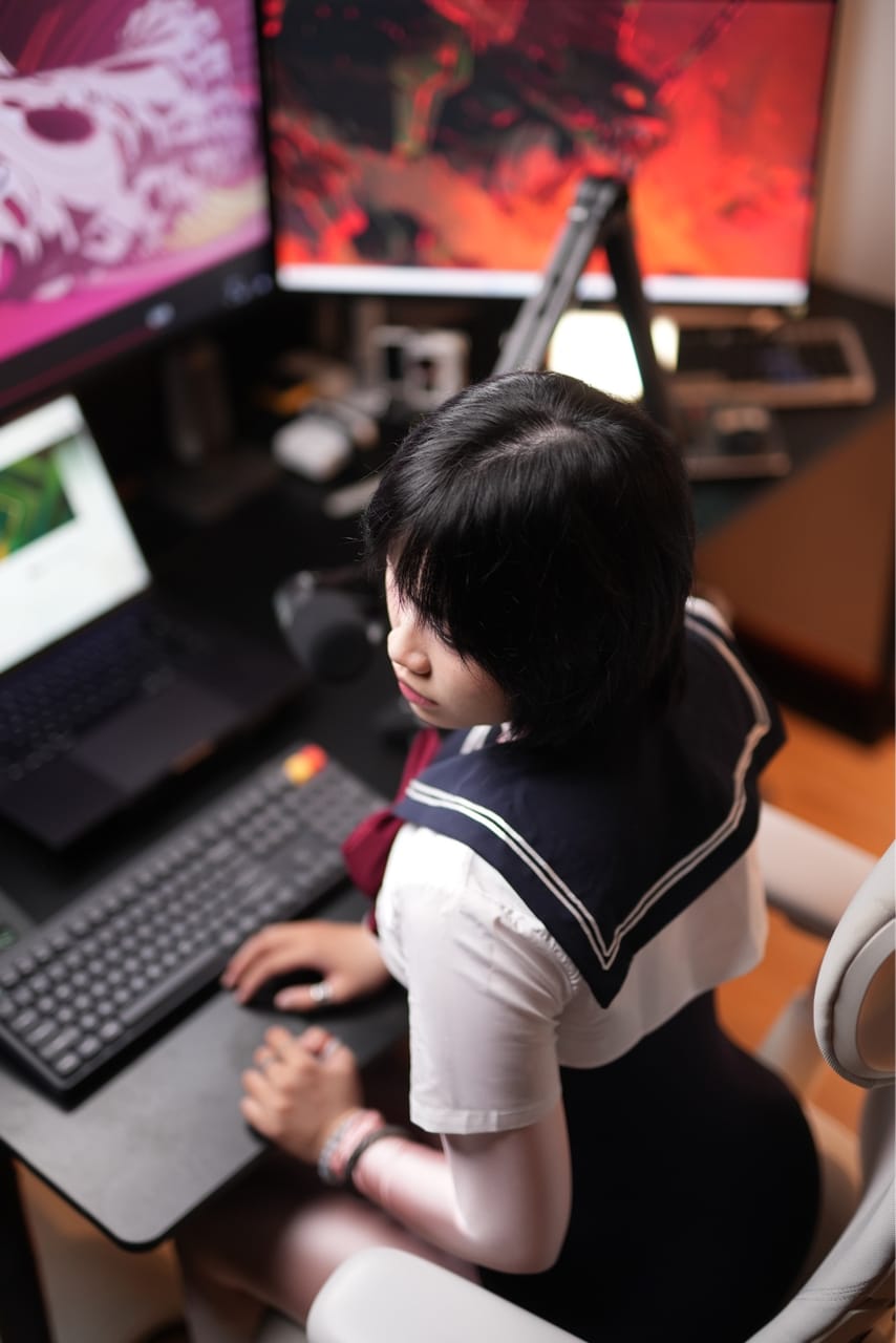 Góc máy của Bảo Dạy Edit: Góc máy tông đen với hai màn hình hình nền đỏ hồng, laptop, micro cần, bàn phím và ghế gaming trắng.
