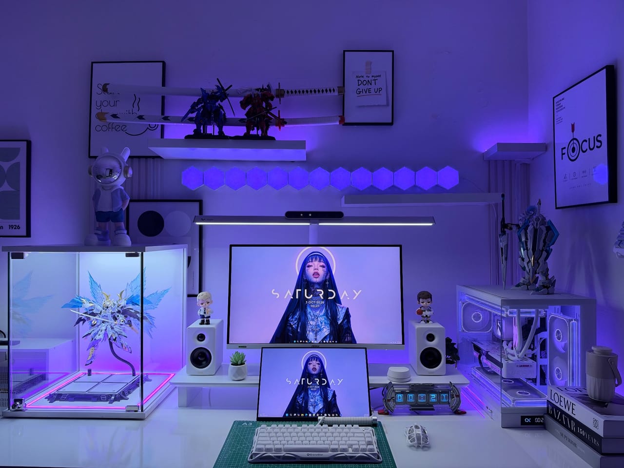 Setup góc máy của Túnn: Góc setup tông trắng với đèn RGB tím xanh, hai màn hình, case kính, loa trắng và nhiều mô hình figure trưng bày.