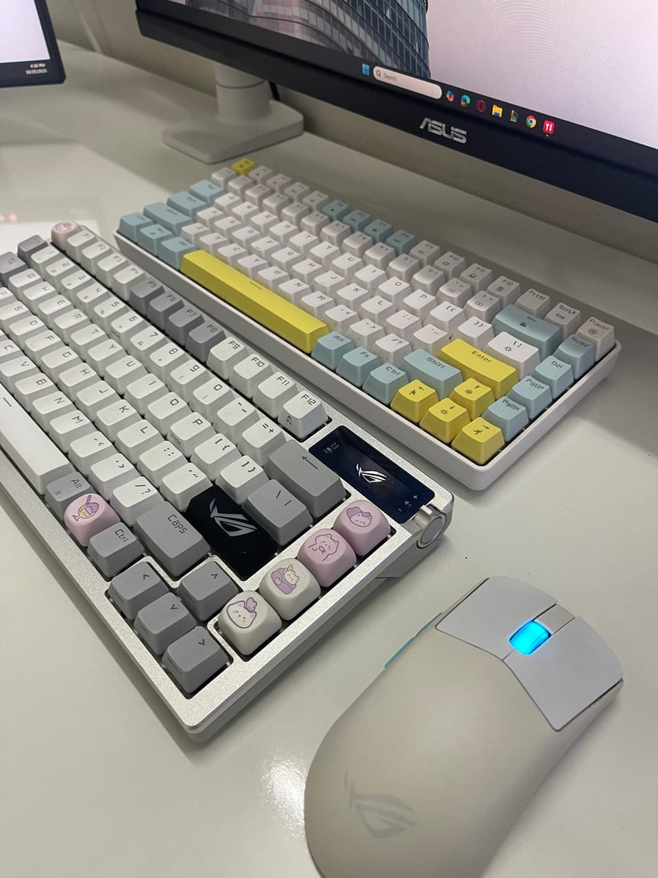 Góc máy của HwangWoo: Góc bàn màu trắng với hai bàn phím cơ keycap pastel, chuột ROG trắng có đèn xanh và màn hình ASUS phía sau.