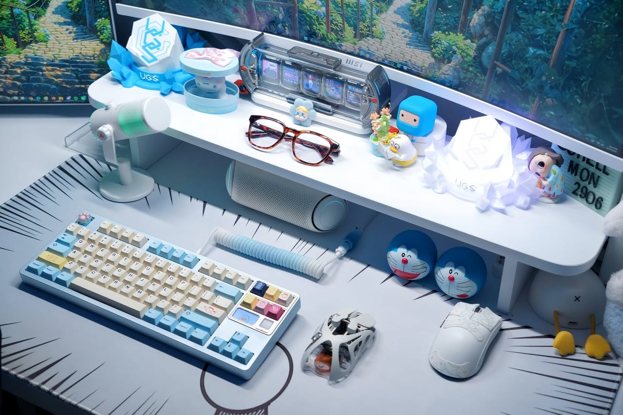 Góc máy của Shellmon: Góc máy tông trắng xanh pastel với kệ đầy mô hình, bàn phím keycap be xanh, hai chuột và lót chuột phong cách manga.