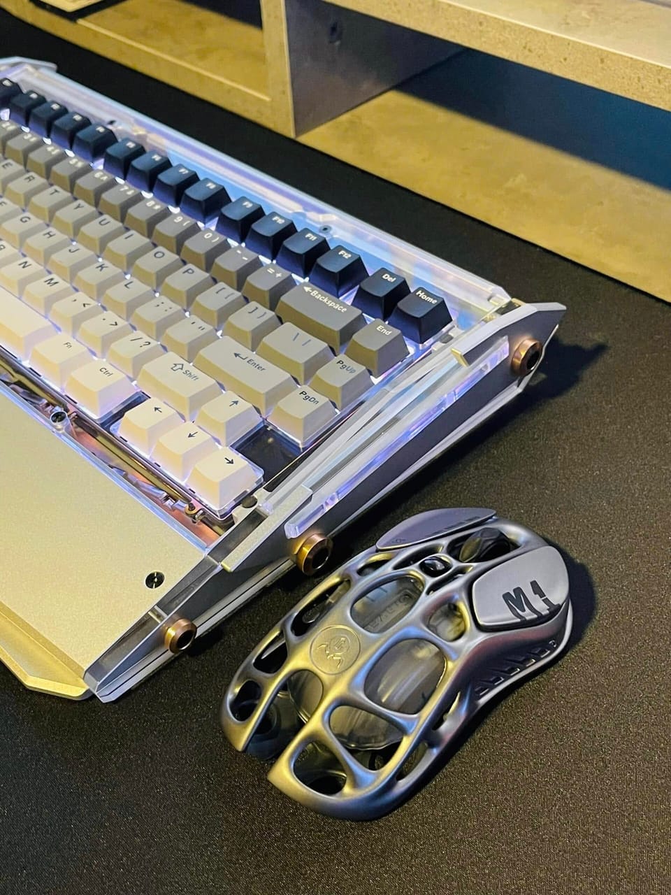 Góc máy của Hieu KU TO: Bàn phím cơ vỏ acrylic trong suốt keycap trắng xám cùng chuột vỏ rỗng kim loại đặt trên lót chuột đen.