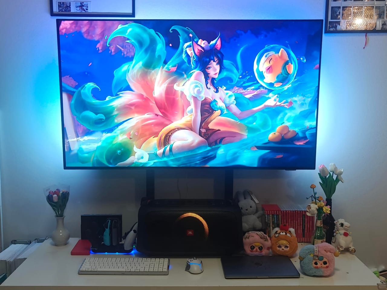 Góc máy của KietVu: Góc bàn trắng với màn hình lớn hiển thị hình anime, đèn nền xanh, loa JBL, bàn phím trắng, laptop, thú bông và hoa tulip.