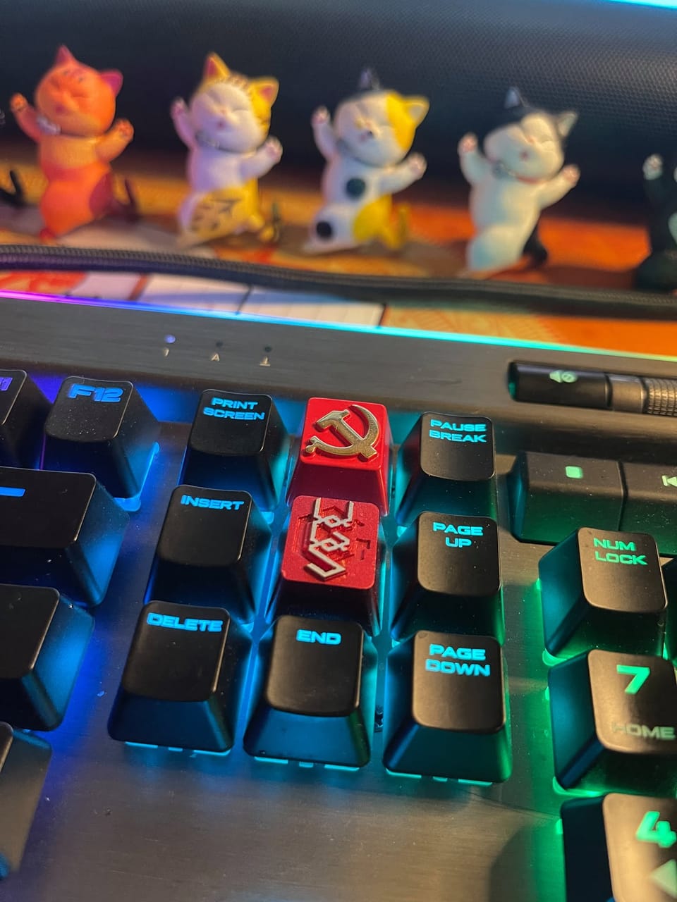Góc máy của Nguyễn Việt Dũng: Cận cảnh bàn phím cơ đèn RGB với hai keycap đỏ kim loại độc đáo, phía sau là hàng mô hình mèo nhỏ đáng yêu.