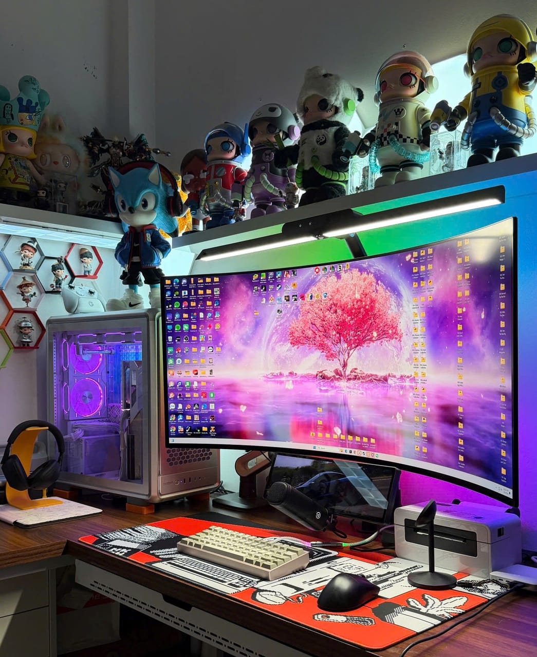 Góc máy của khachoang: Góc máy với màn hình cong ultrawide hình nền hoa anh đào, case trắng đèn tím, bàn phím kem và dàn figure trưng bày phía trên.