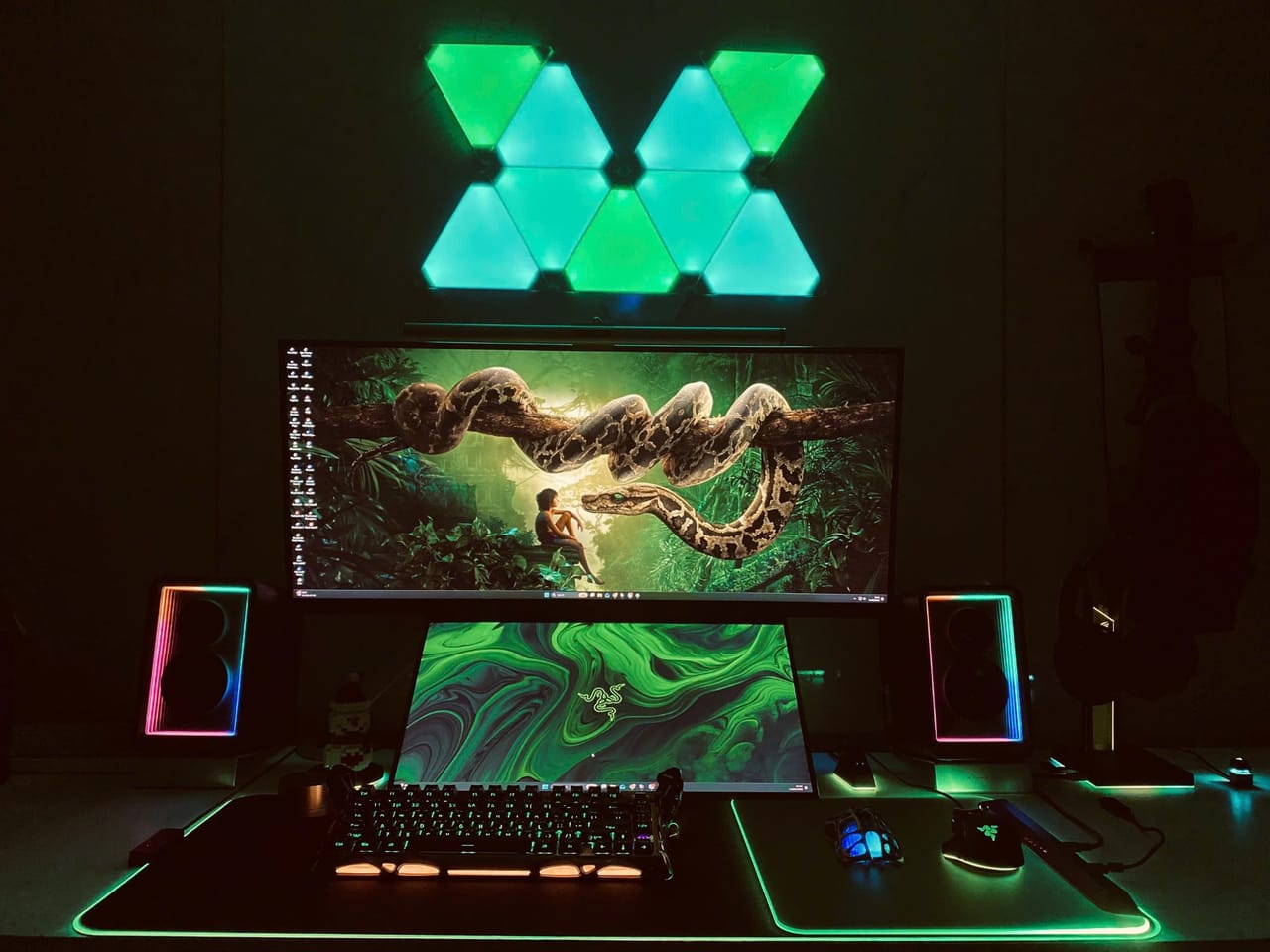 Setup góc máy của Tony Quân: Góc máy tối với đèn panel tường, hai màn hình, loa và lót chuột RGB, tông xanh lá chủ đạo rất đậm chất gaming.
