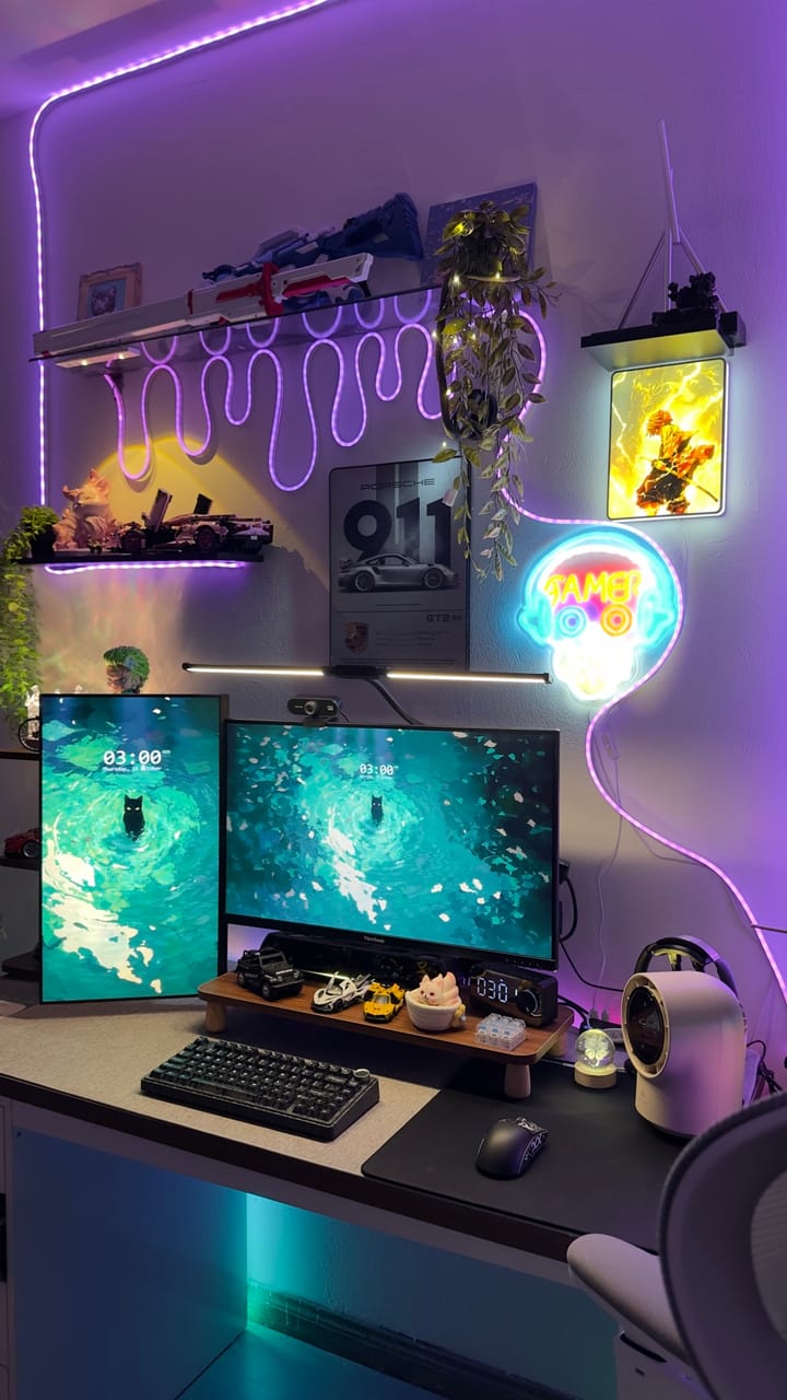 Góc máy của Kaii: Góc máy neon tím rực rỡ với hai màn hình, một màn dựng dọc, kèm mô hình xe, figure anime và cây xanh.