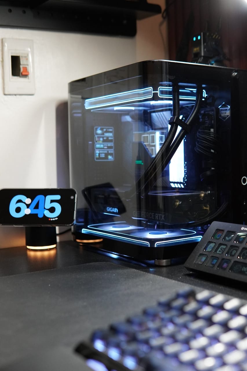 Góc máy của Kenzihaisan: Case PC kính cong đèn viền xanh neon, card RTX bên trong, cạnh bàn phím LED và bàn phím macro trên bàn đen.