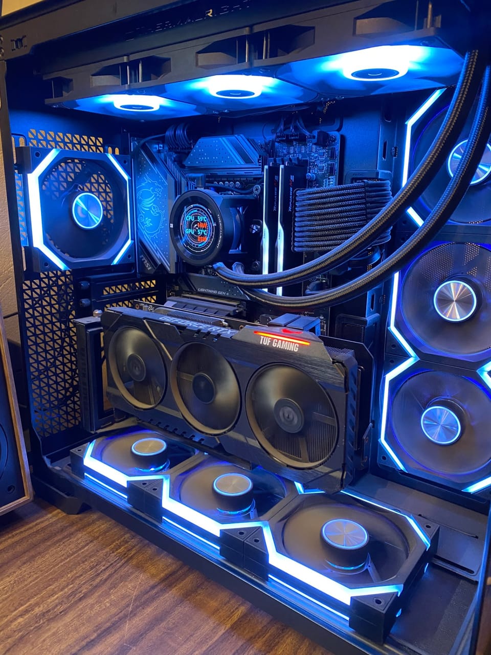 Góc máy của Ngô Đức Minh: Bên trong case PC kính cong màu đen với dàn quạt LED xanh dương, card đồ họa TUF Gaming và tản nhiệt nước AIO có màn hình.