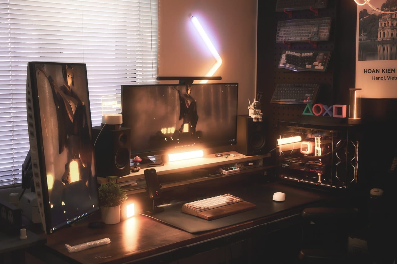 Góc máy của DuongLinh: Góc máy tối ánh đèn cam ấm với hai màn hình, PC case trong suốt, loa, micro và bàn phím trưng bày trên tường.
