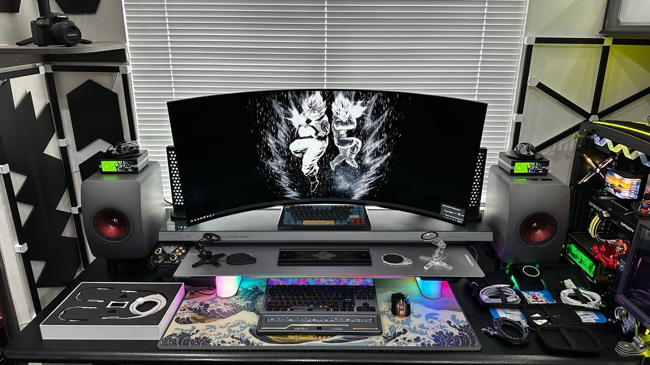 Góc máy của Đức Cương: Góc máy tông đen xám với màn hình cong siêu rộng, cặp loa bookshelf, bàn phím RGB, lót chuột sóng Nhật và nhiều phụ kiện cáp.