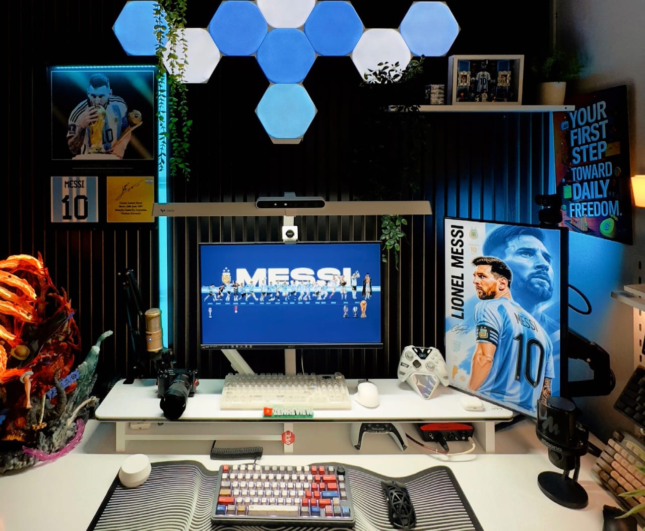 Setup góc máy của Drake nè: Góc bàn trắng đèn nền xanh dương với đèn lục giác, hai màn hình, micro, bàn phím cơ, mô hình anime và đồ trang trí bóng đá.