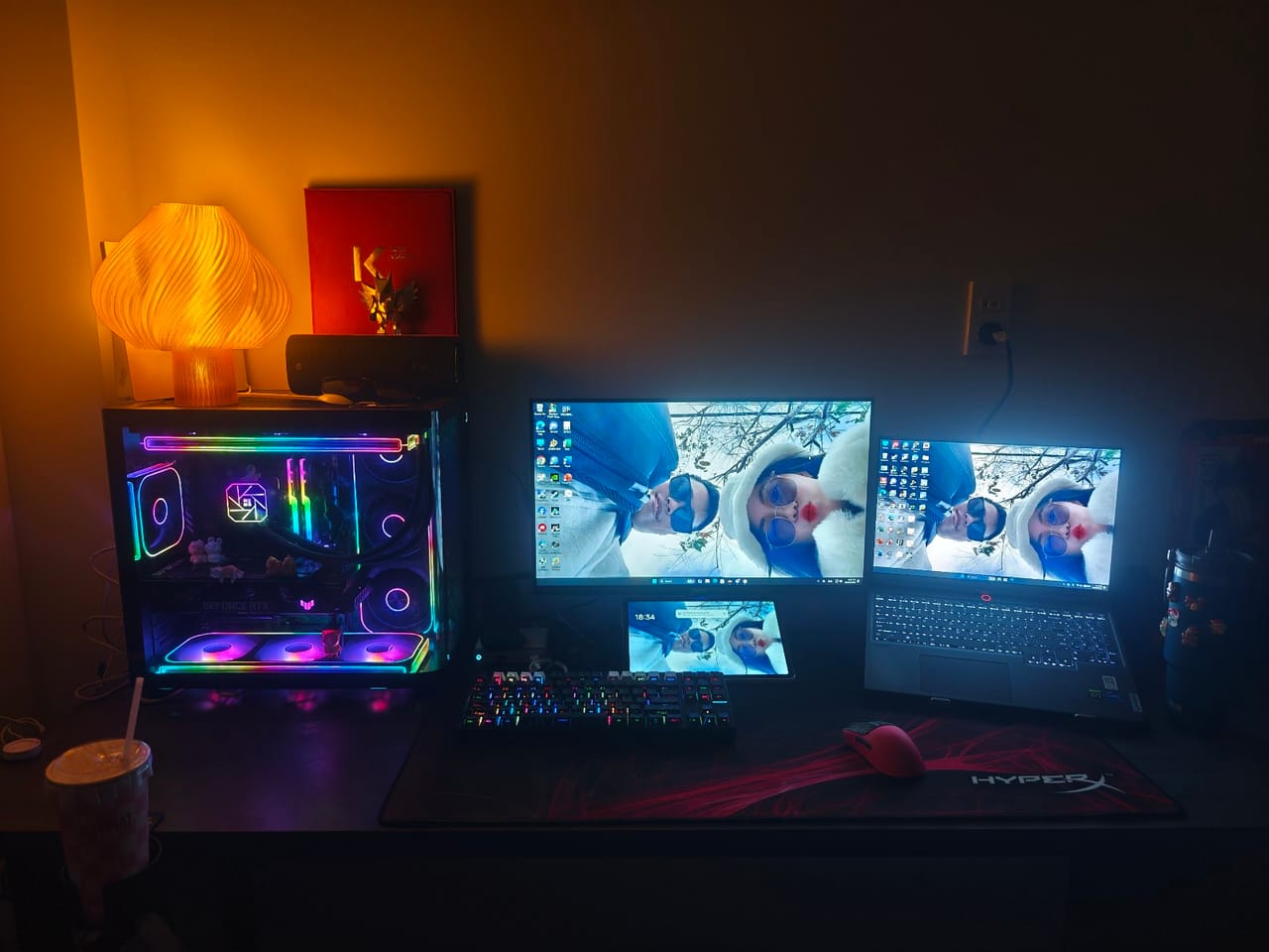 Góc máy của Comi0610: Góc máy tối với case kính LED RGB rực rỡ, màn hình, laptop, máy tính bảng, bàn phím RGB và đèn nấm cam ấm áp.