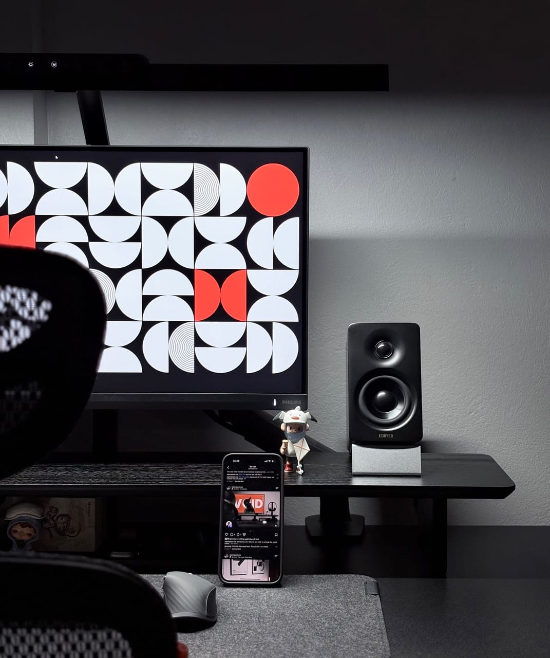 Góc máy của Junchan: Góc bàn tông đen xám tối giản với màn hình Philips hiển thị hình nền hình học đỏ trắng, loa Edifier, điện thoại và figure nhỏ.