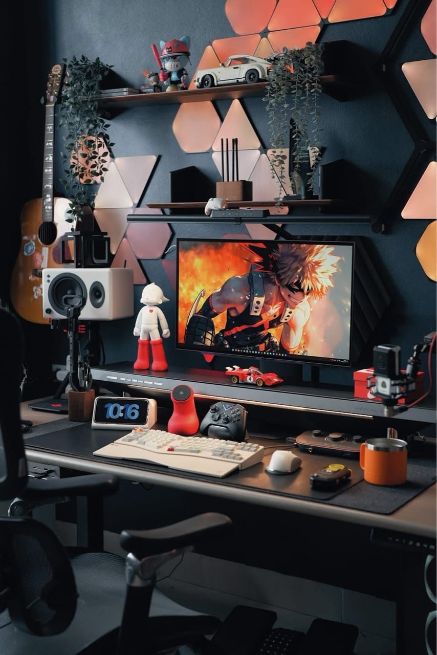 Góc máy của Xung Quanh Trung: Góc máy tông đen cam với đèn panel hình học, figure anime, mô hình xe, cây xanh và guitar treo tường.