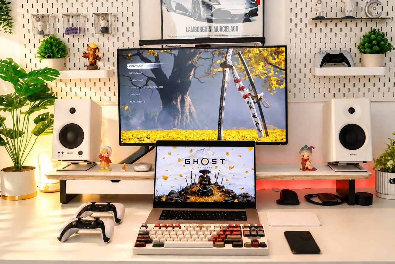 Góc máy của Ghost Strike: Góc setup tông trắng ấm áp với pegboard, cây xanh, loa Edifier, màn hình và laptop đang chạy Ghost of Yōtei, kèm tay cầm DualSense.