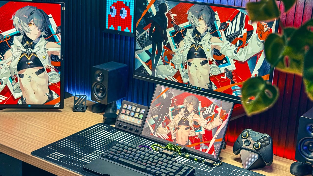 Góc máy của Anh Già: Góc máy tông đen đỏ với ba màn hình cùng hình nền anime, loa Edifier, tay cầm chơi game, đèn LED và chậu cây xanh.