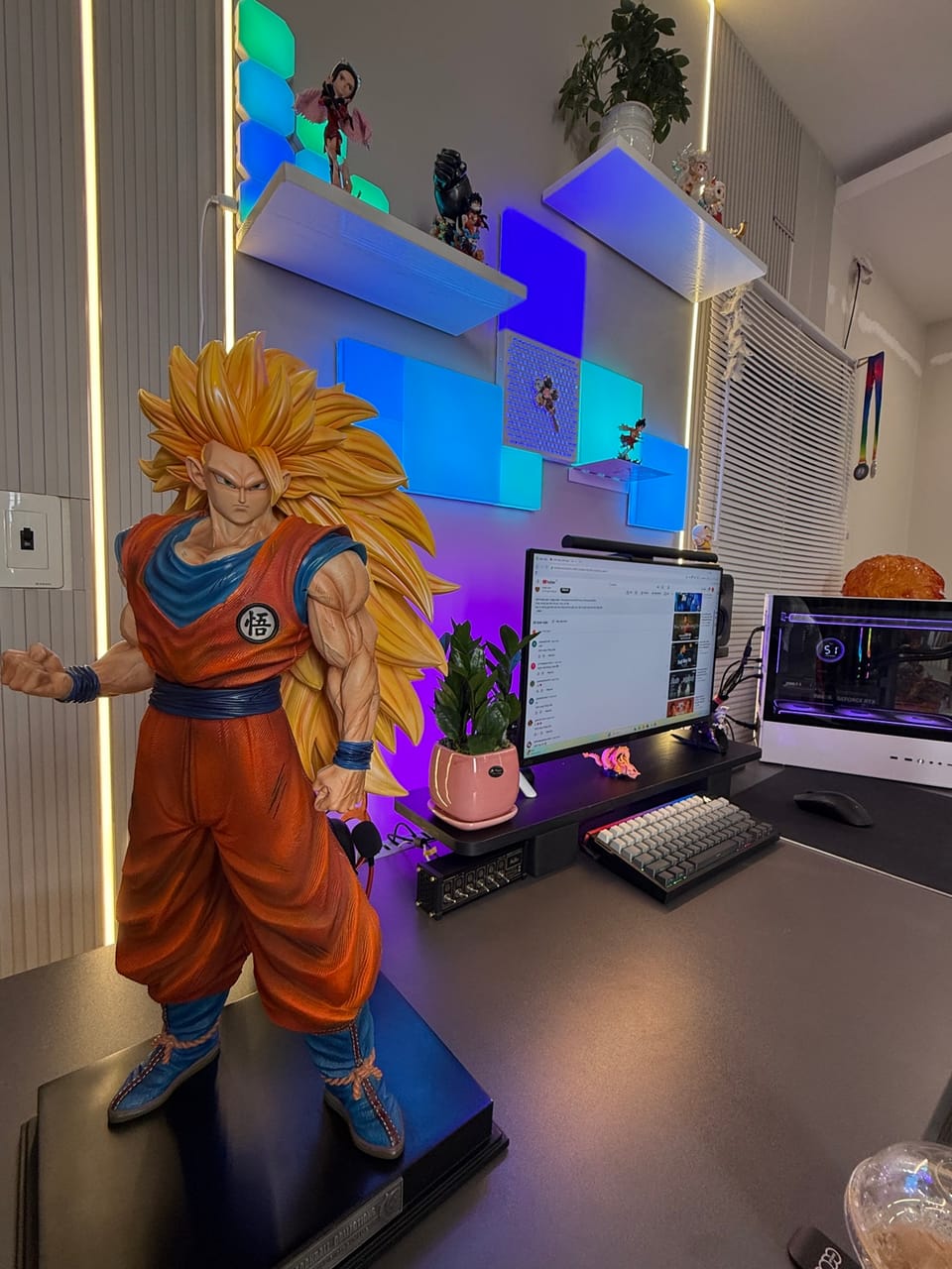 Góc máy của Thưởng: Góc máy anime với tượng Goku SSJ3 cỡ lớn, đèn LED ô vuông tím xanh, kệ figure và cây xanh.