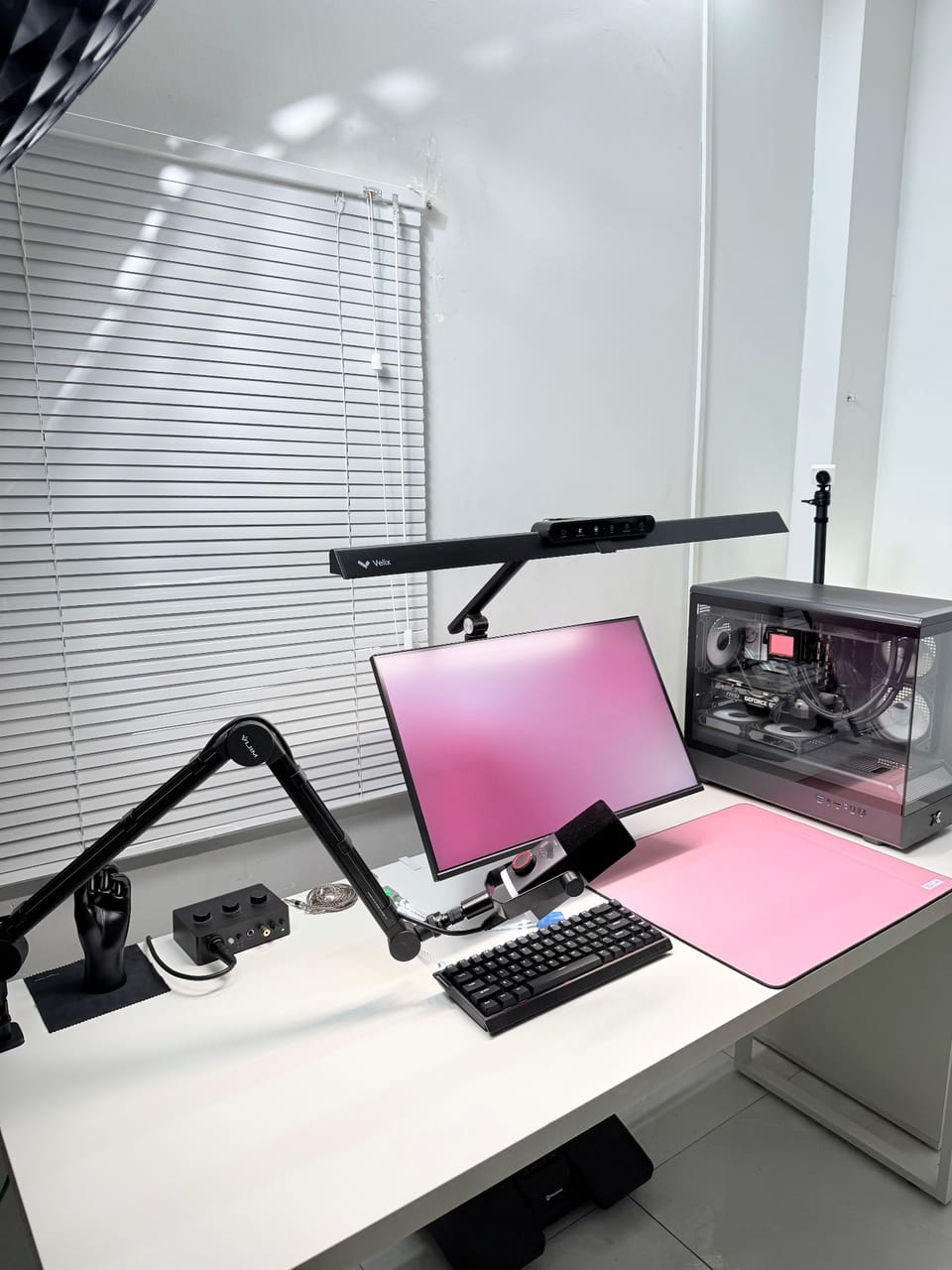 Góc máy của Intdire: Góc setup trắng đen điểm nhấn hồng pastel với màn hình, đèn treo màn hình, micro có arm, bàn phím và case PC kính trong suốt.