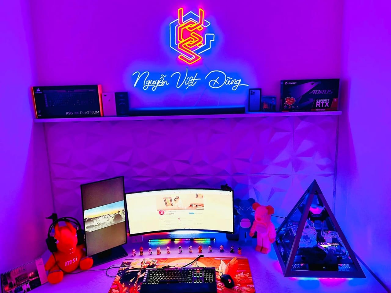 Góc máy của Nguyễn Việt Dũng: Góc máy ánh đèn tím neon với màn hình cong, màn hình dọc, case kim tự tháp, bàn phím RGB và nhiều mô hình trang trí.