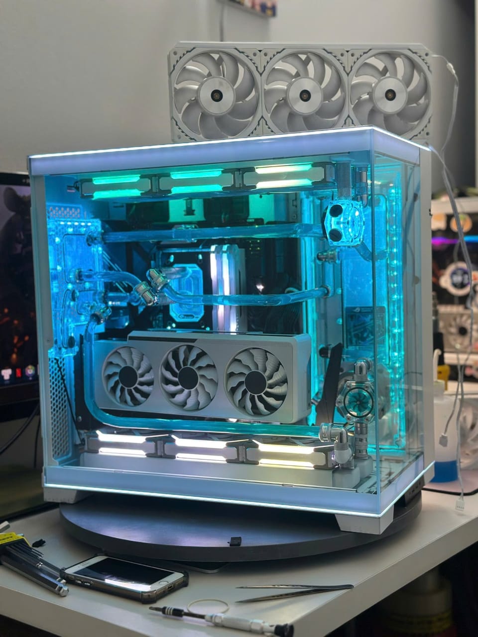 Góc máy của ReaperAlphaXVII: Dàn PC vỏ kính màu trắng tản nhiệt nước custom, đèn LED xanh ngọc rực rỡ, đặt trên bàn xoay cùng dụng cụ lắp ráp.