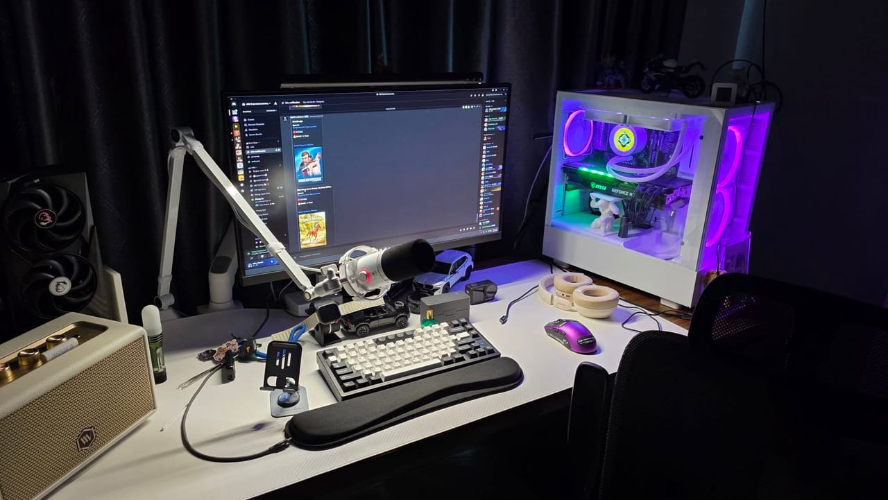Góc máy của dtran2k: Góc máy tông trắng đen với PC tản nhiệt nước đèn RGB tím, micro livestream, bàn phím cơ, chuột tím và loa retro.