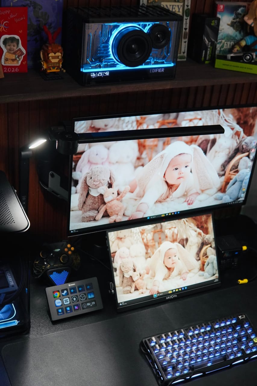 Góc máy của Kenzihaisan: Góc bàn tông đen với loa Edifier đèn neon xanh, hai màn hình, Stream Deck, bàn phím cơ LED xanh và kệ gỗ trưng bày đồ.