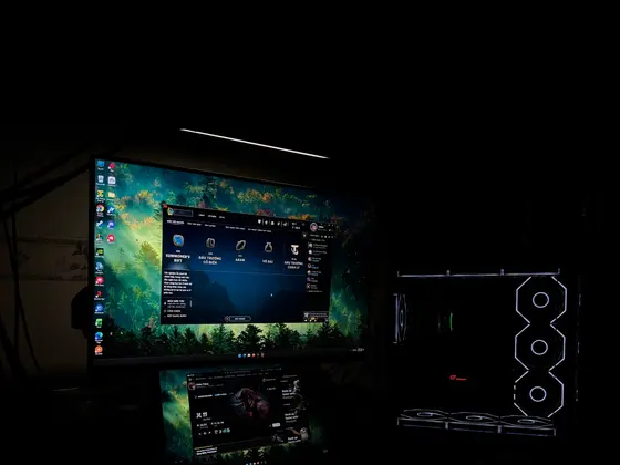 Góc máy của Vinh Lê: Góc máy tối với hai màn hình xếp chồng đang mở League of Legends, case kính quạt LED trắng và đèn treo màn hình.