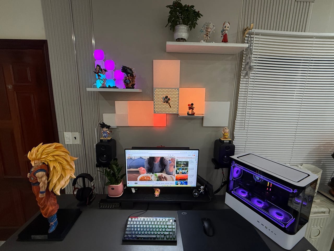 Góc máy của Thưởng: Góc máy tông xám trắng với đèn panel trang trí, case PC LED tím và nhiều figure Dragon Ball, One Piece nổi bật.