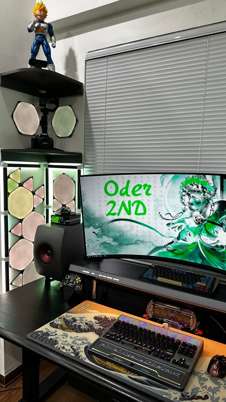 Góc máy của Đức Cương: Góc setup tông đen với màn hình cong, hai bàn phím cơ, loa để bàn, đèn lục giác phát sáng và mô hình anime trên kệ góc.