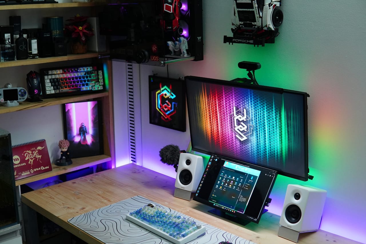 Góc máy của double_q: Góc bàn gỗ sáng với đèn LED RGB tím xanh, hai màn hình, loa trắng, bàn phím cơ và kệ trưng bày mô hình.