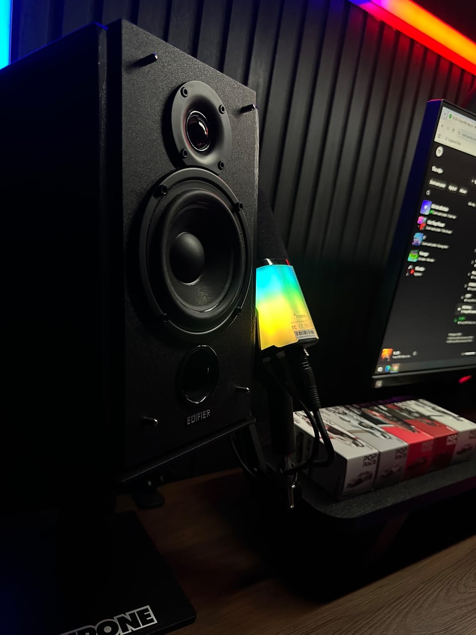 Góc máy của supra27: Góc bàn tối với loa Edifier màu đen, đèn RGB nhiều màu bên cạnh, màn hình phía sau và hộp mô hình xe Pop Race.