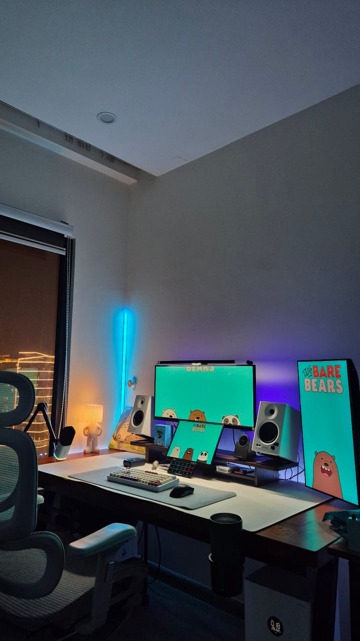 Góc máy của Khánh99: Góc bàn làm việc buổi tối với ba màn hình hình nền We Bare Bears, loa trắng, đèn LED xanh tím và ghế công thái học.