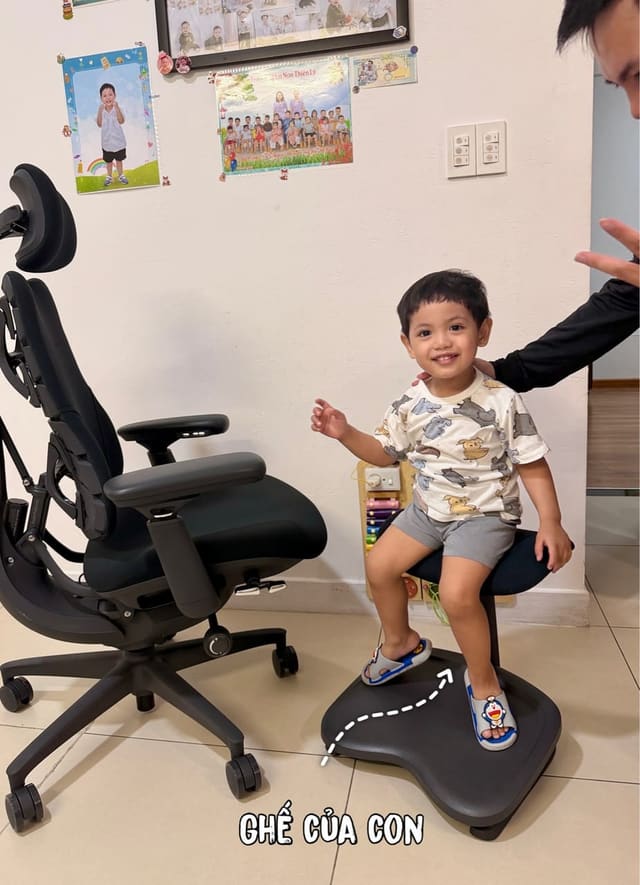 Chiếc ghế công thái học màu đen cạnh một chiếc ghế nhỏ dành cho trẻ em trong góc nhà, không có bàn hay máy tính.